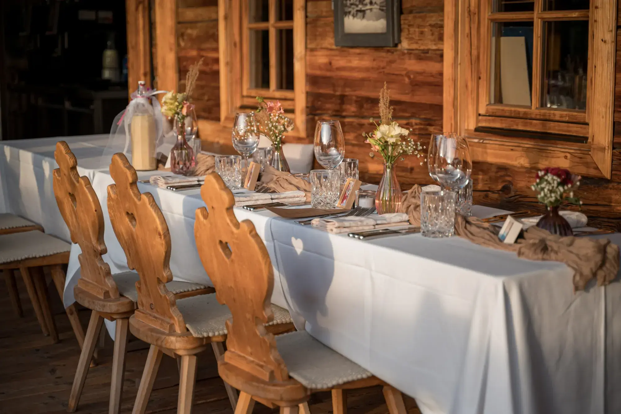 Festlich gedeckte Tafel mit geschnitzten Tiroler Holzstühlen und Blumengestecken vor der Almhütte der Stöttlalm in Mieming