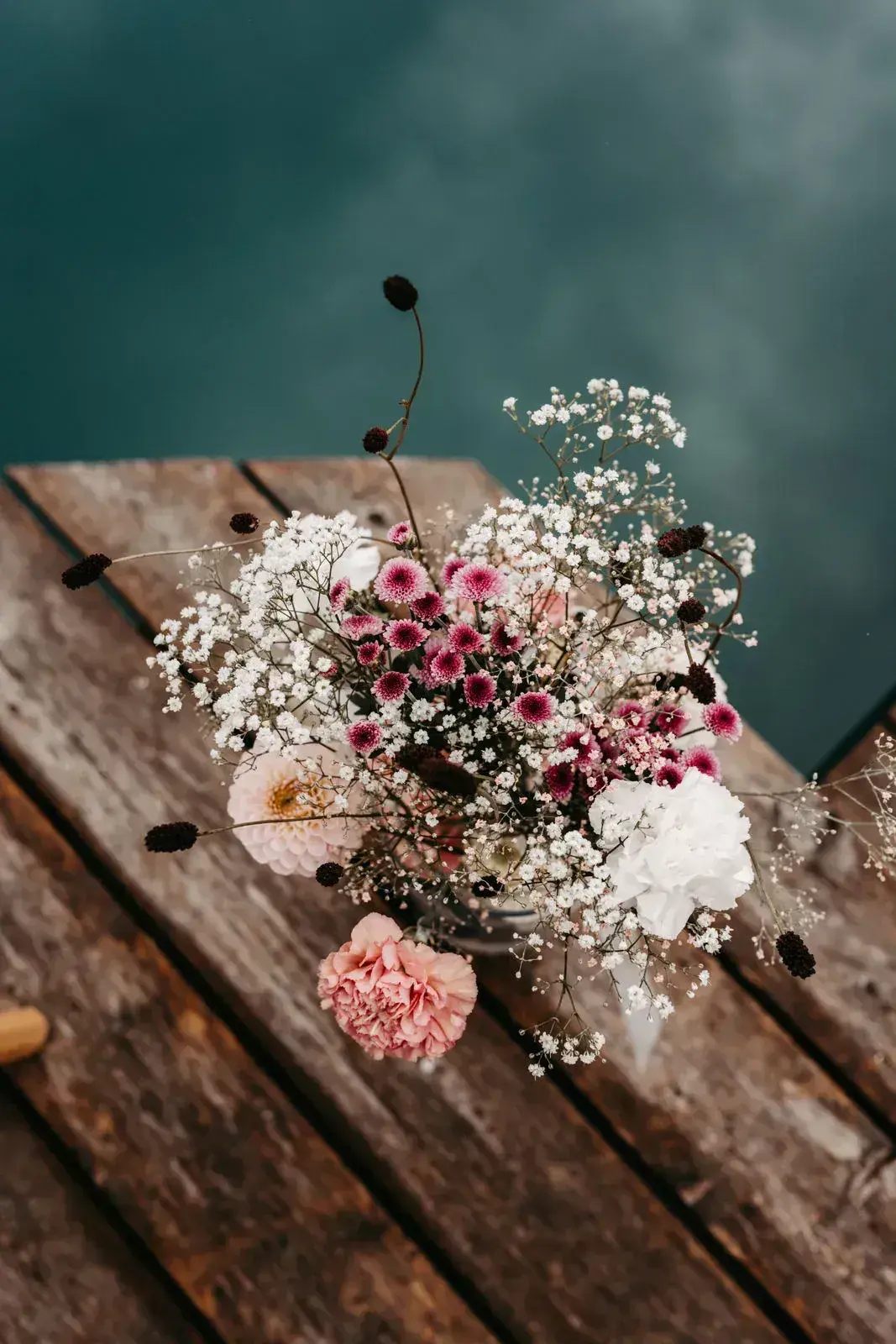 Zarter Brautstrauß aus rosa und weißen Blüten mit Schleierkraut auf einem Holzsteg über dem türkisfarbenen Stöttlalmsee