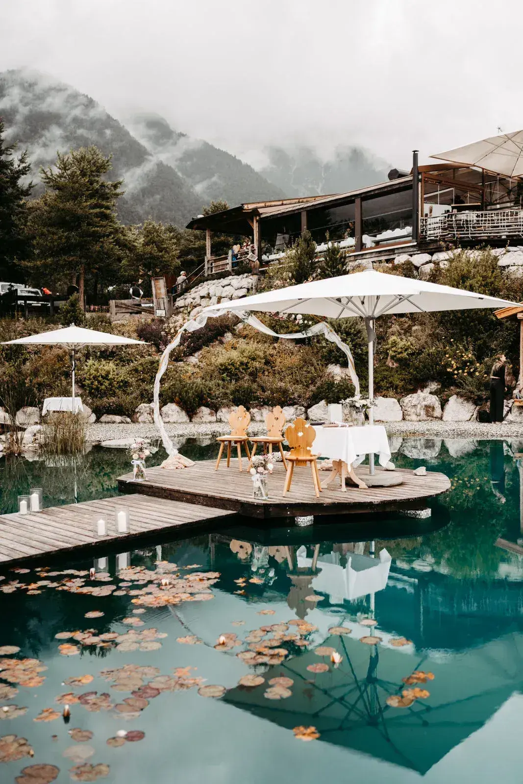 Festlich gedeckte Hochzeitstafel mit Sonnenschirmen und Pampasgras auf dem Holzsteg am Stöttlalmsee vor der nebelverhangenen Mieminger Kette