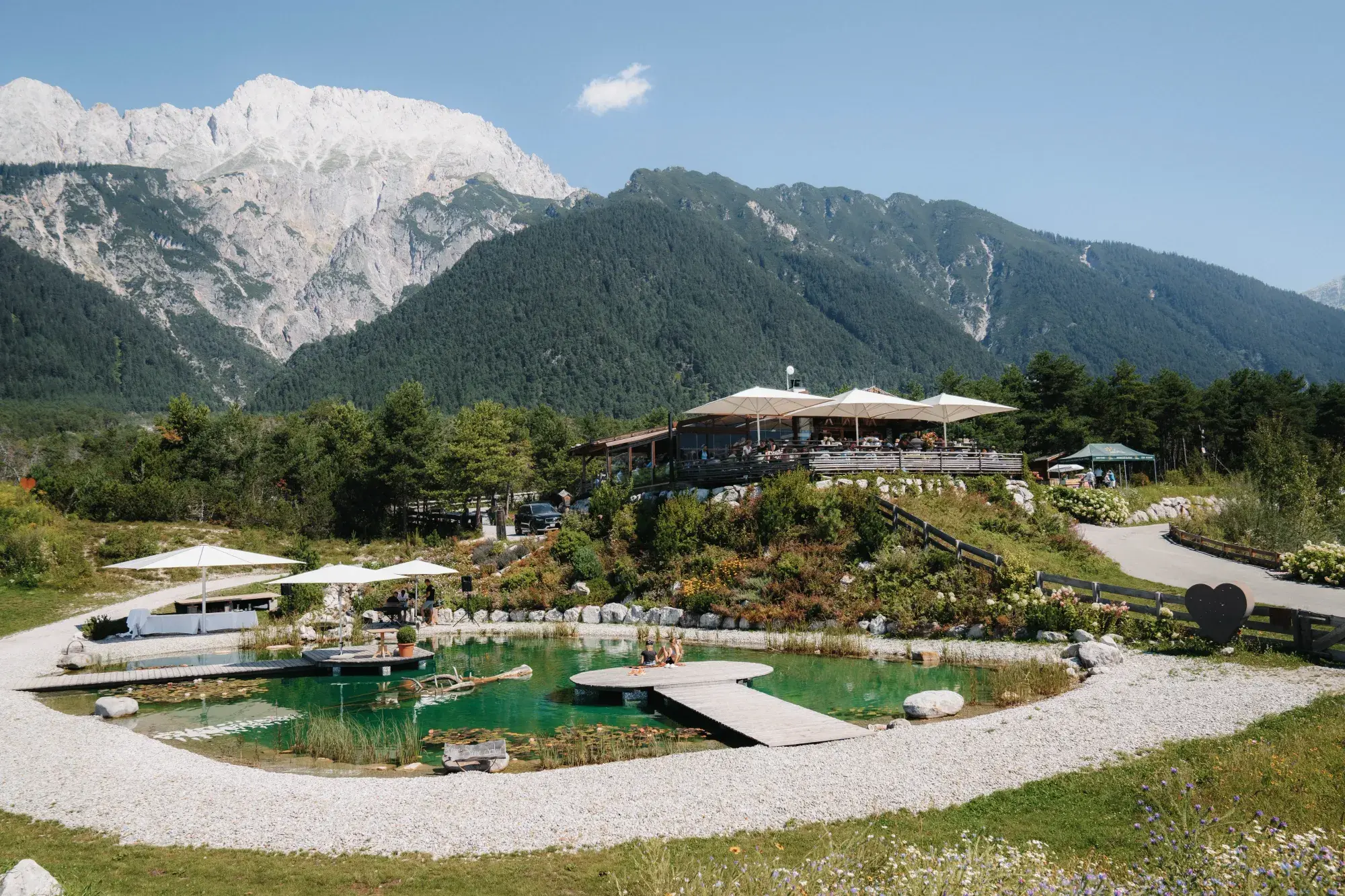 Sommerliche Gesamtansicht der Hochzeitslocation Stöttlalm mit Sonnenterrasse und Naturbadeteich Stöttlalmsee vor der Mieminger Kette