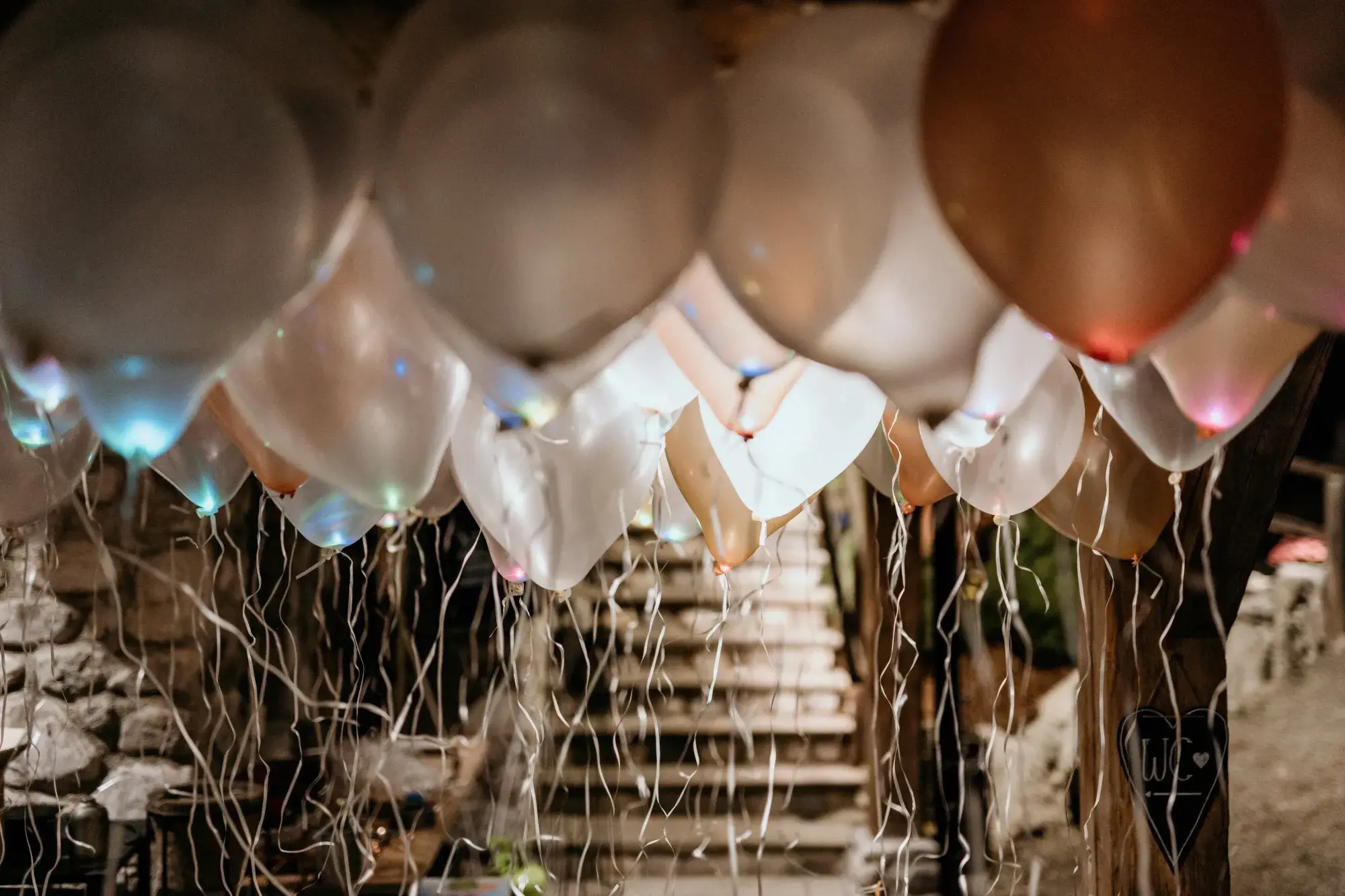 LED-beleuchtete Luftballons in Weiß- und Kupfertönen schweben am Abend über einer steinernen Treppe bei einer Feier an der Stöttlalm
