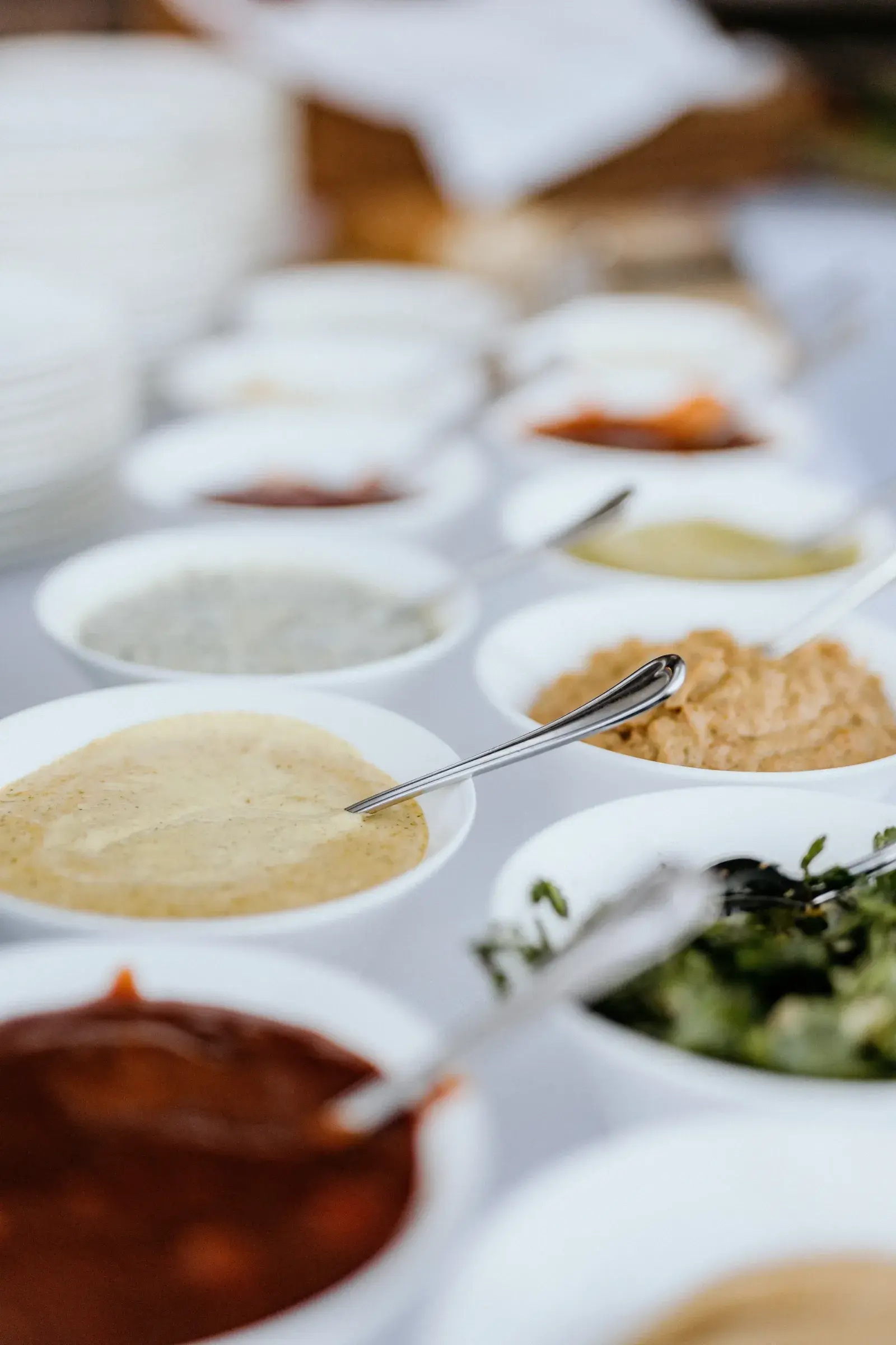 Reihe weißer Schälchen mit hausgemachten Saucen, Dips und Aufstrichen auf einem festlich gedeckten Buffet der Stöttlalm