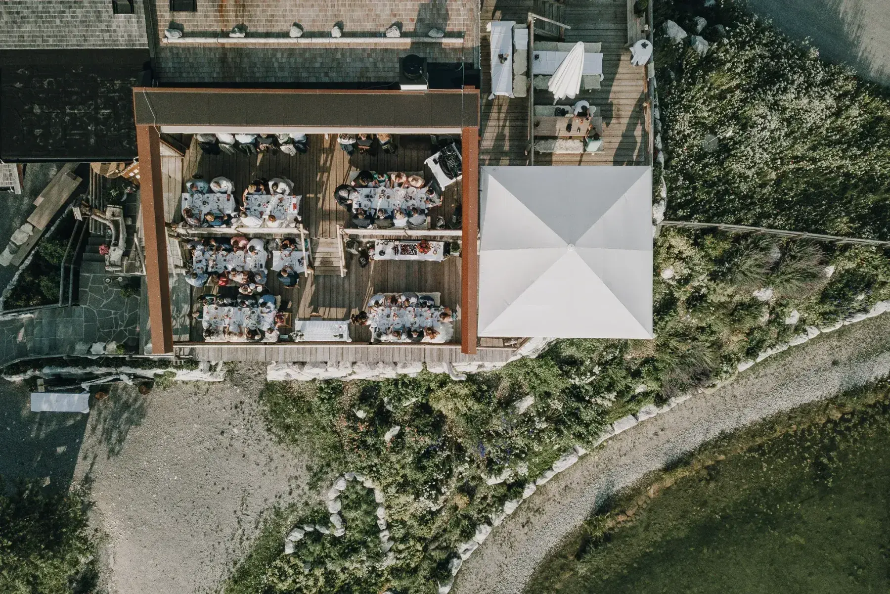 Luftaufnahme senkrecht auf die überdachte Terrasse der Stöttlalm mit langen, festlich gedeckten Hochzeitstafeln und zahlreichen Gästen